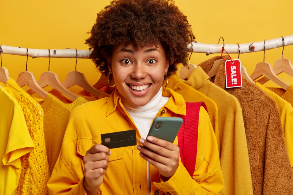 Mulher sorrindo segurando um cartão de crédito e celular, simbolizando as oportunidades de vendas na Shein com promoções e produtos atrativos