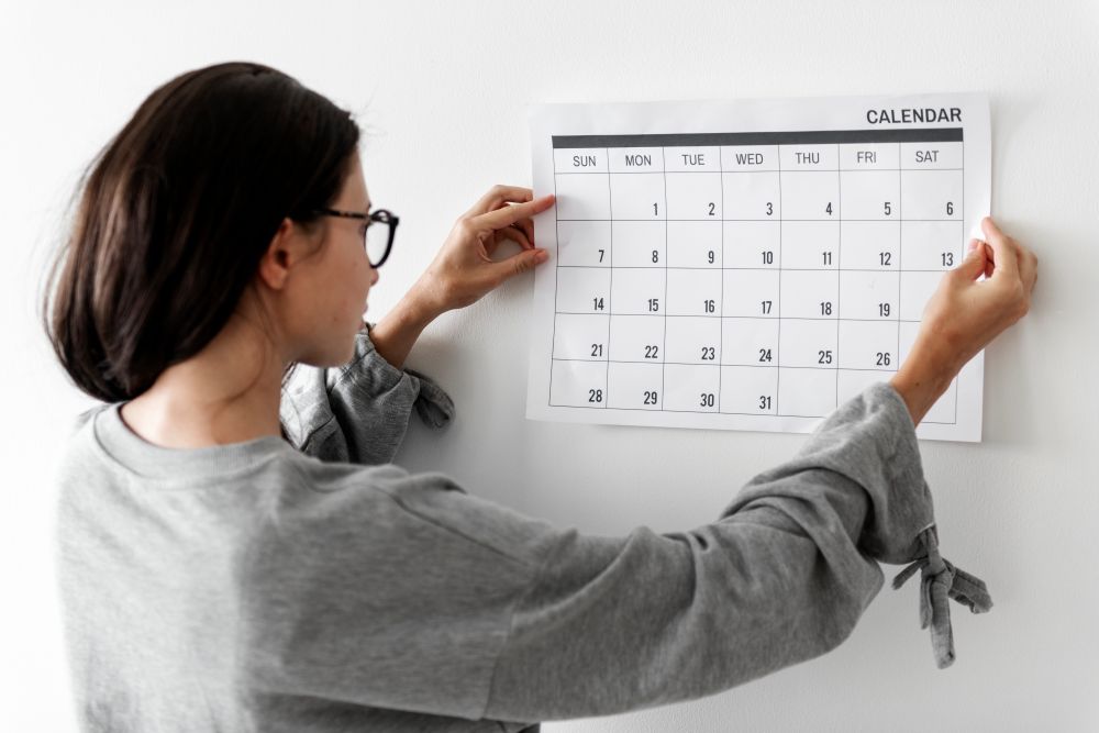 Mulher organizando um calendário mensal na parede, representando planejamento de campanhas e datas comemorativas para e-commerce.
