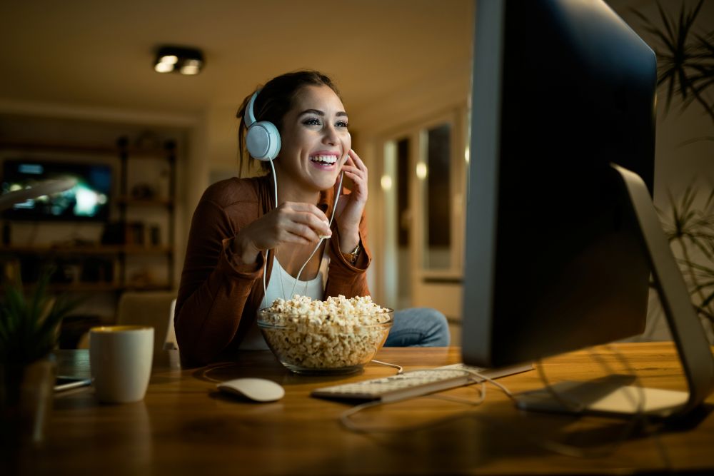 Mulher assistindo a filme sobre empreendedorismo no computador enquanto anota ideias, representando aprendizado e inspiração para negócios.